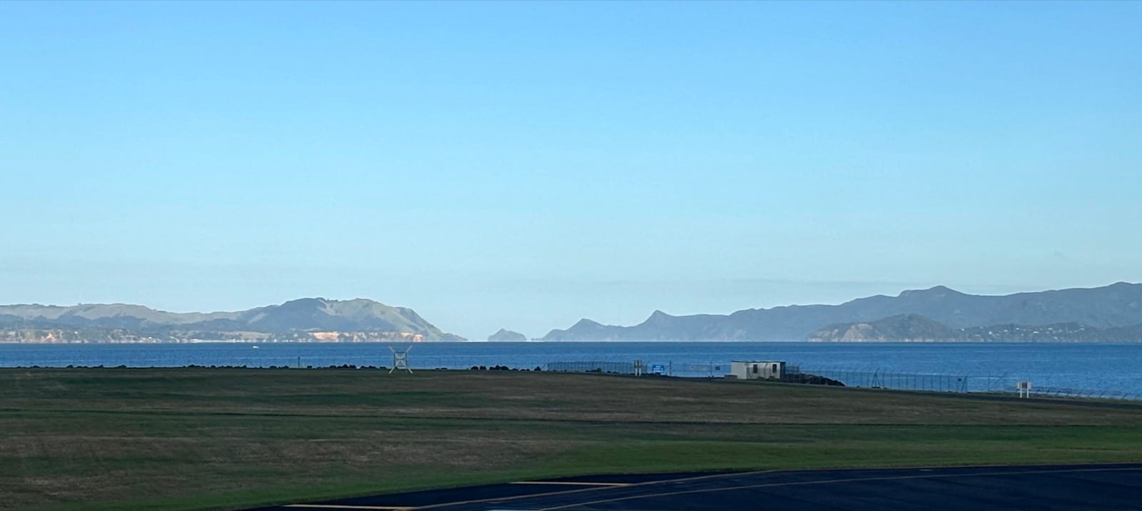 Manukau Heads and the harbour entrance seen across grass flats from the Awhitu side.