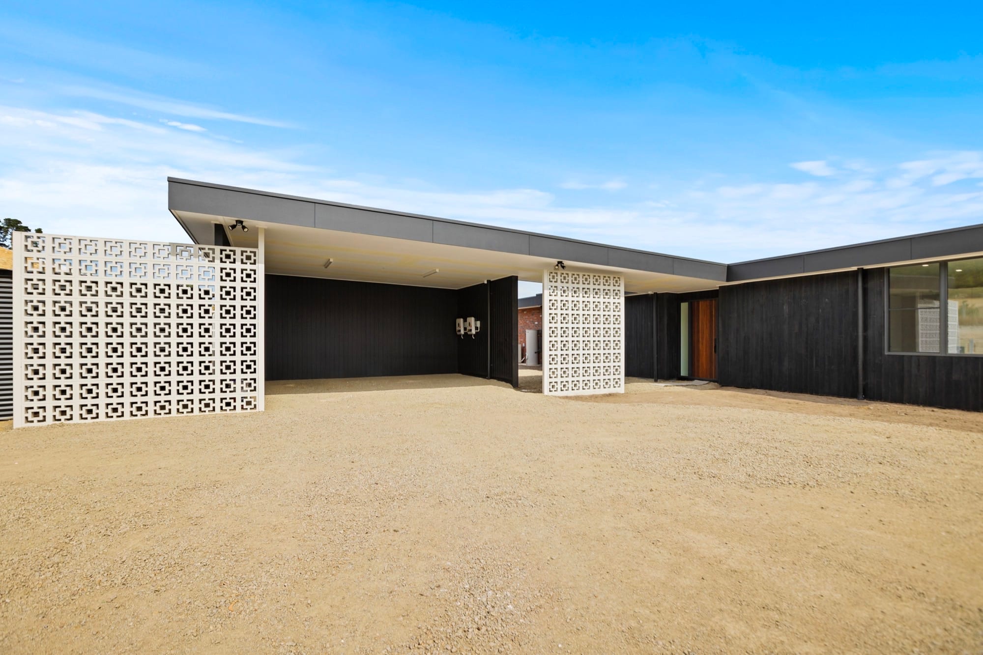 A carport and outbuilding clad in dark timber with a breeze-block screen wall.
