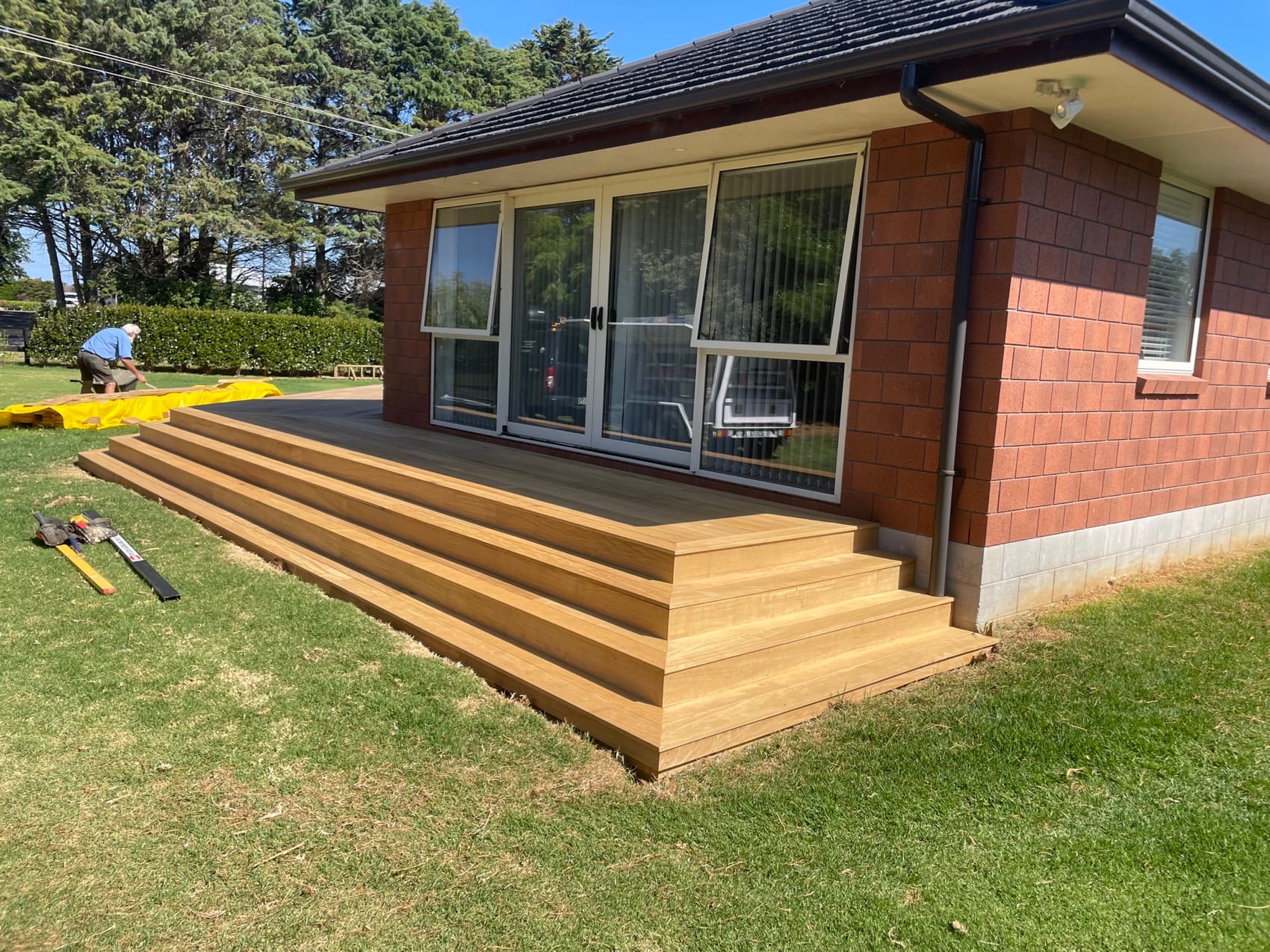 A finished Backline Construction deck with wide timber steps running the length of a brick house.