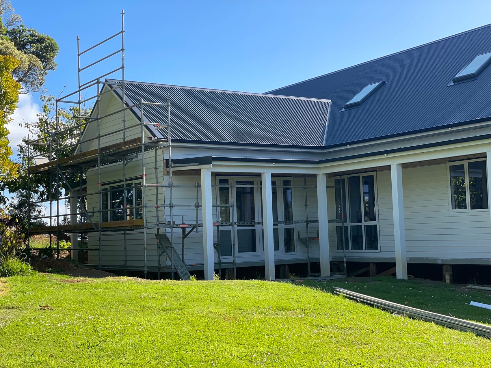 A large weatherboard homestead lifted and supported on temporary posts, scaffolded, during major structural work.
