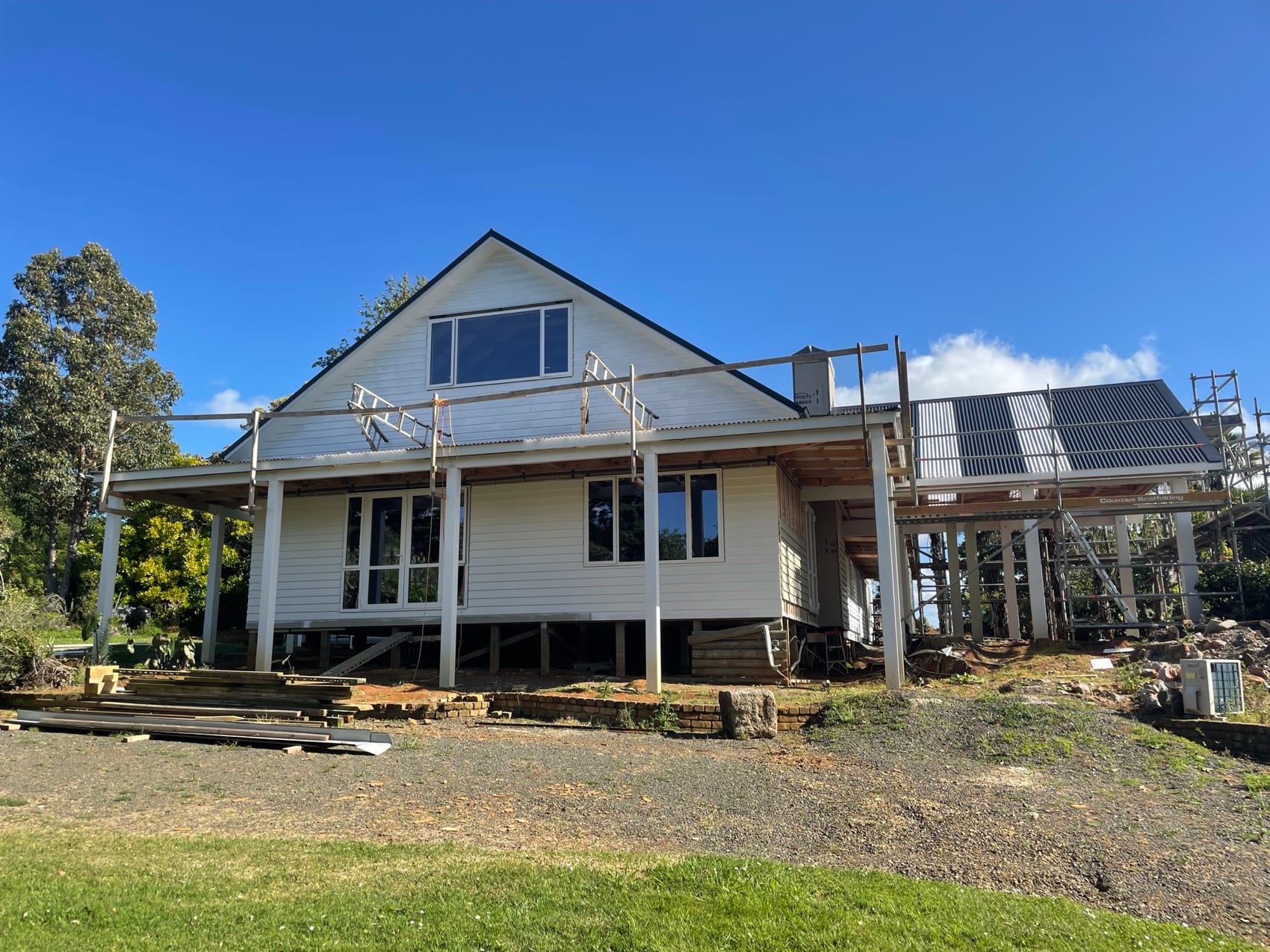 The rear of a raised homestead with new sub-floor structure in place and scaffolding around the upper storey.