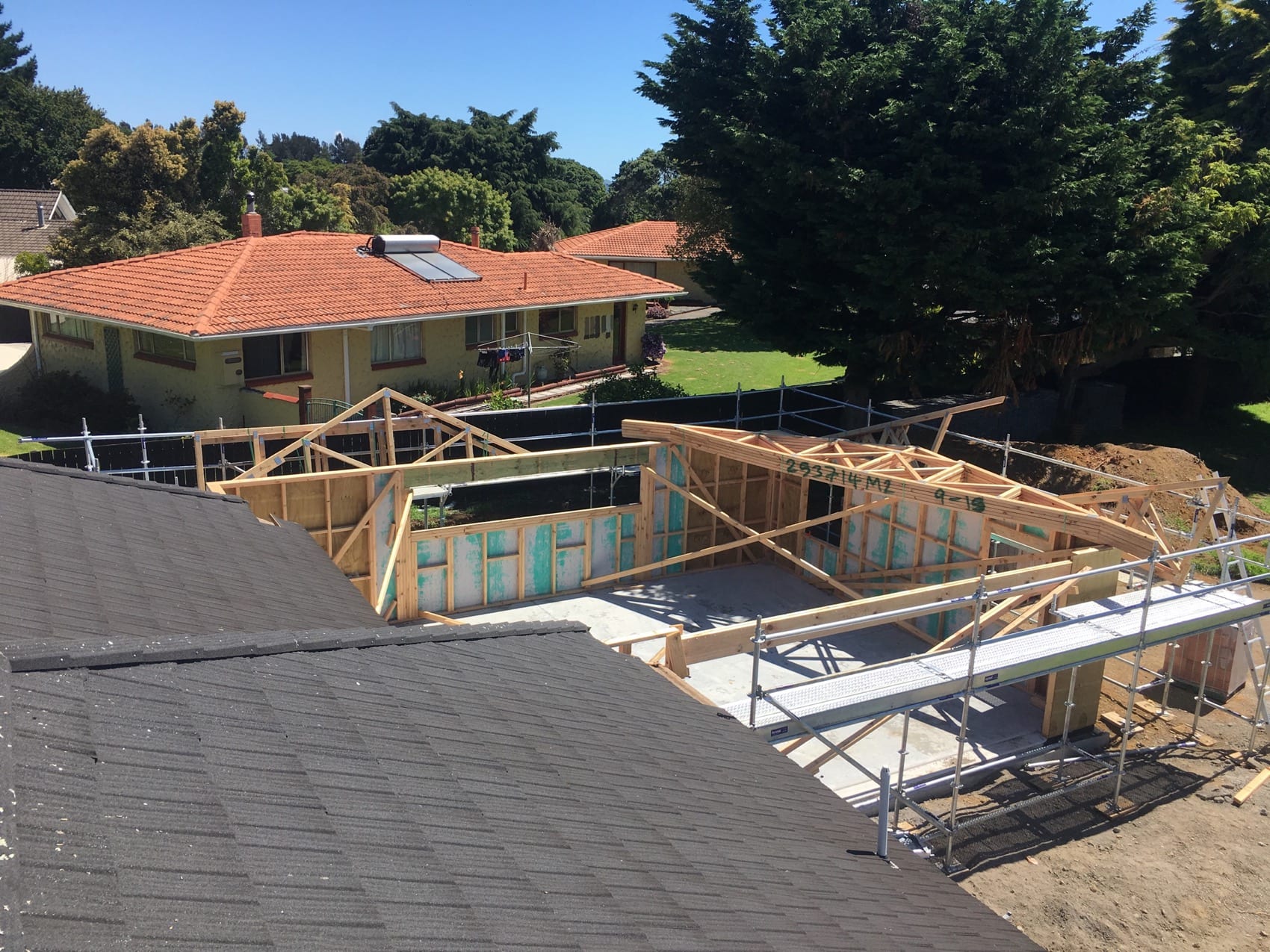 New framing rising beside an existing tiled roof, showing where the addition meets the original house.