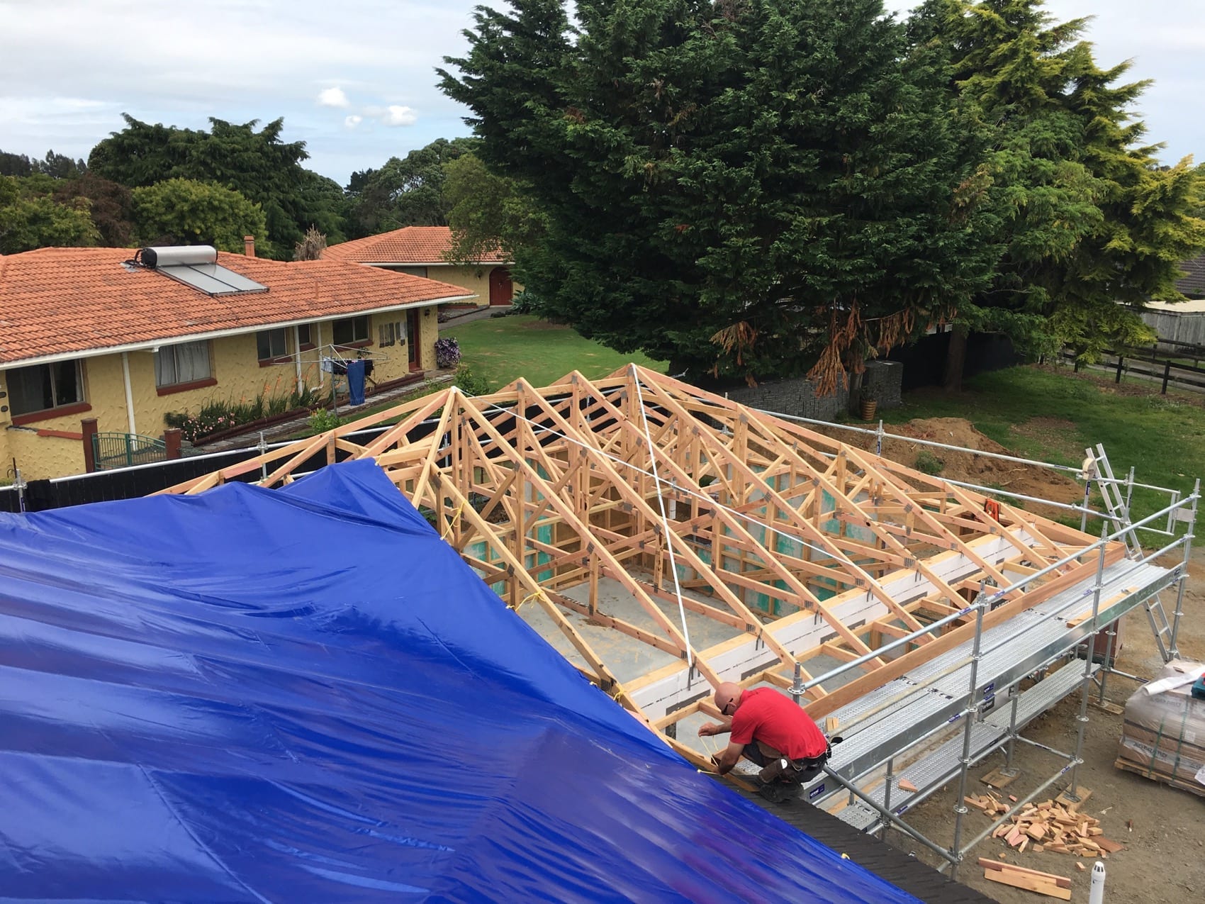 New roof framing over an extension, tarped against weather while the roof is closed in.