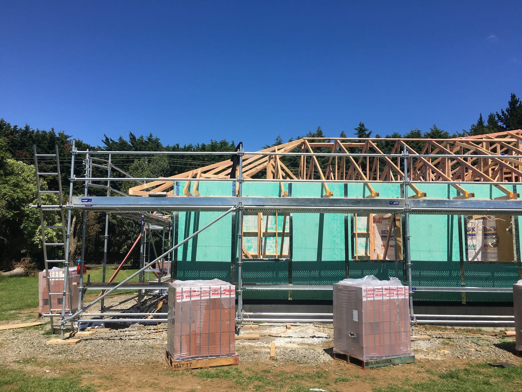 A new wing being framed onto an existing house, wrapped and scaffolded, with the original roof still in place alongside.