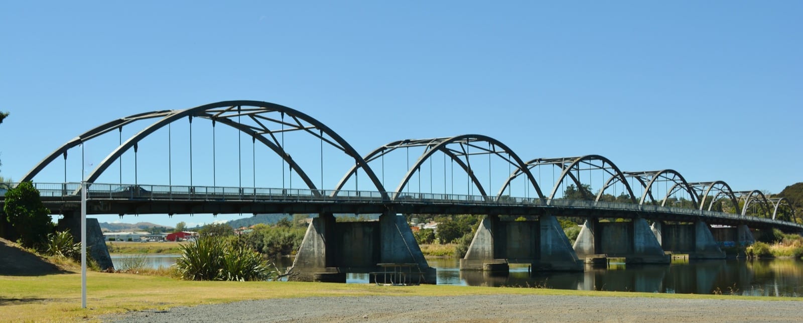 The steel arches of Tainui Bridge crossing the Waikato River at Huntly, wide panorama.