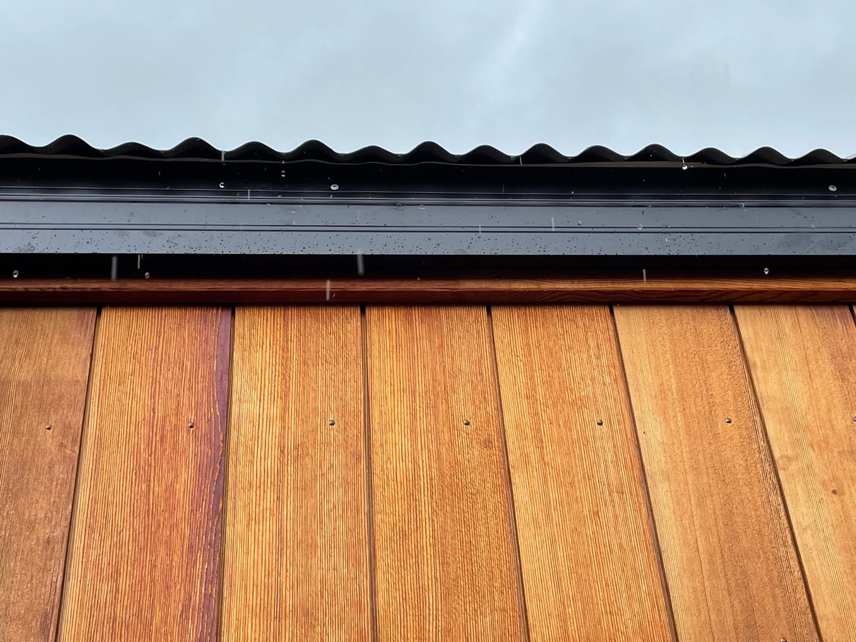 Vertical cedar cladding boards fixed and lapped, seen close.