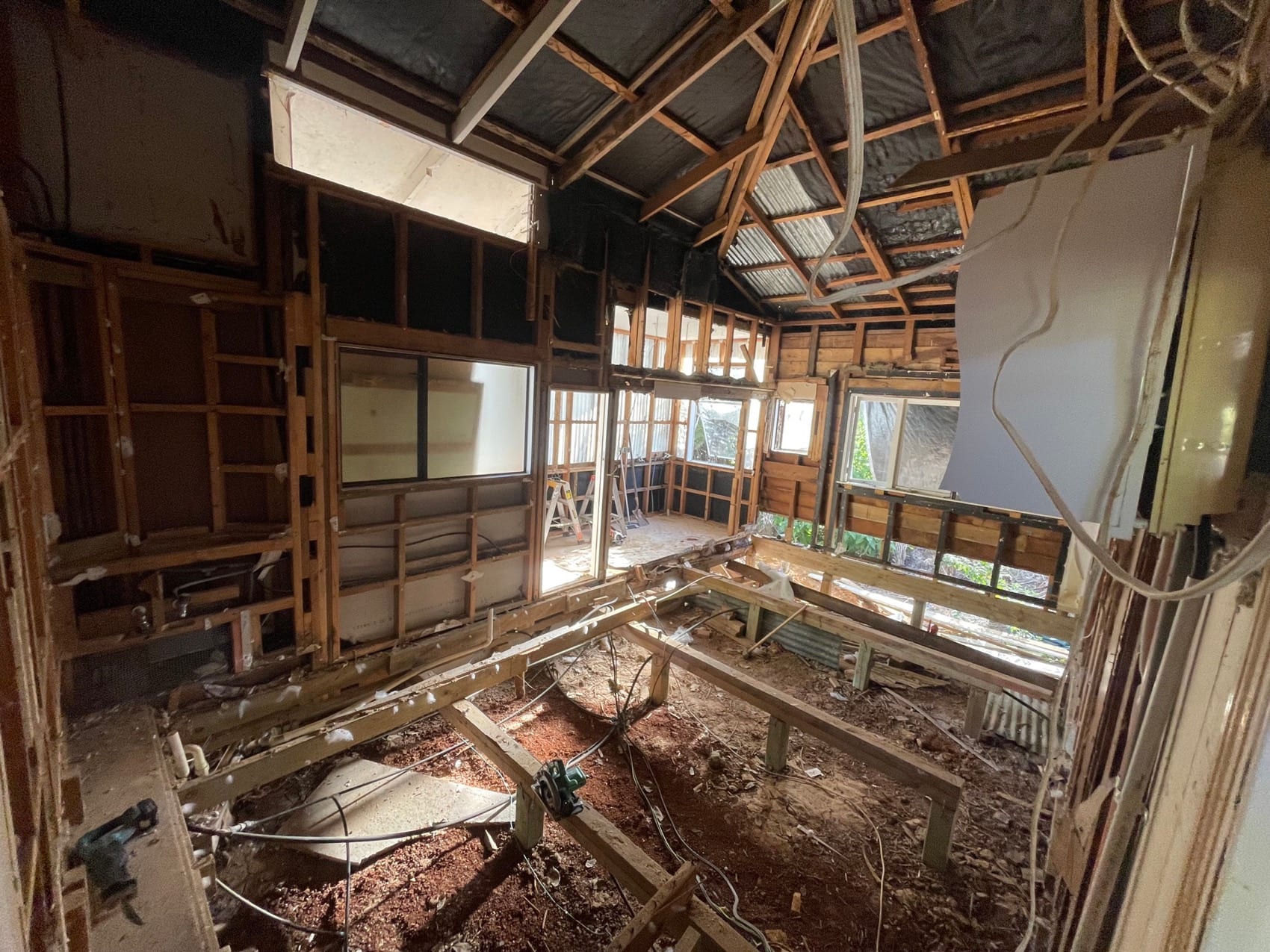 A villa interior mid strip-out, ceilings open to the rafters and old linings removed back to framing.