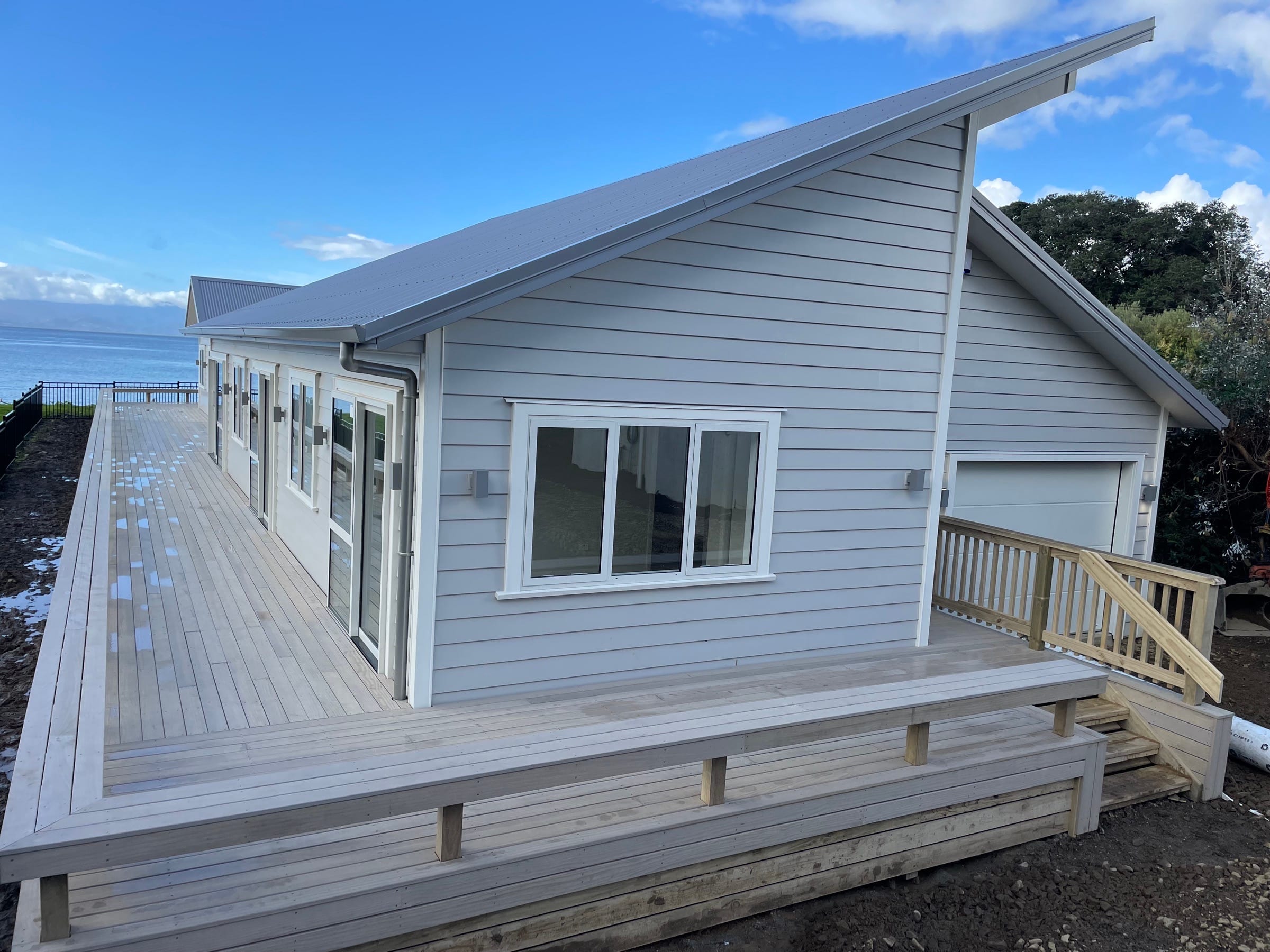 A weatherboard home built by Backline Construction on a coastal site, with a wrap-around deck and balustrade looking out to the water.