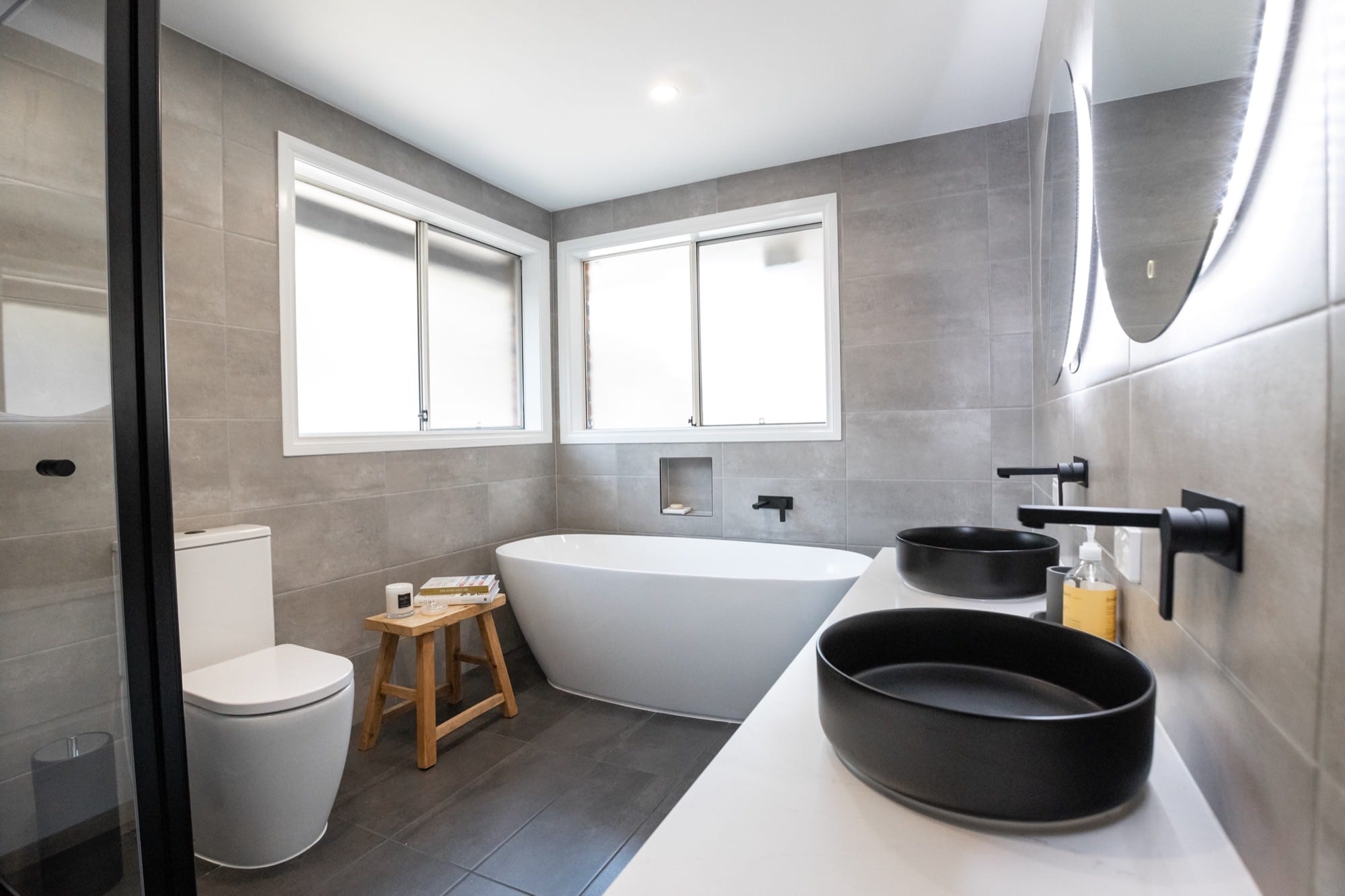 A bathroom with a freestanding tub, concrete-look tiling and a large window.