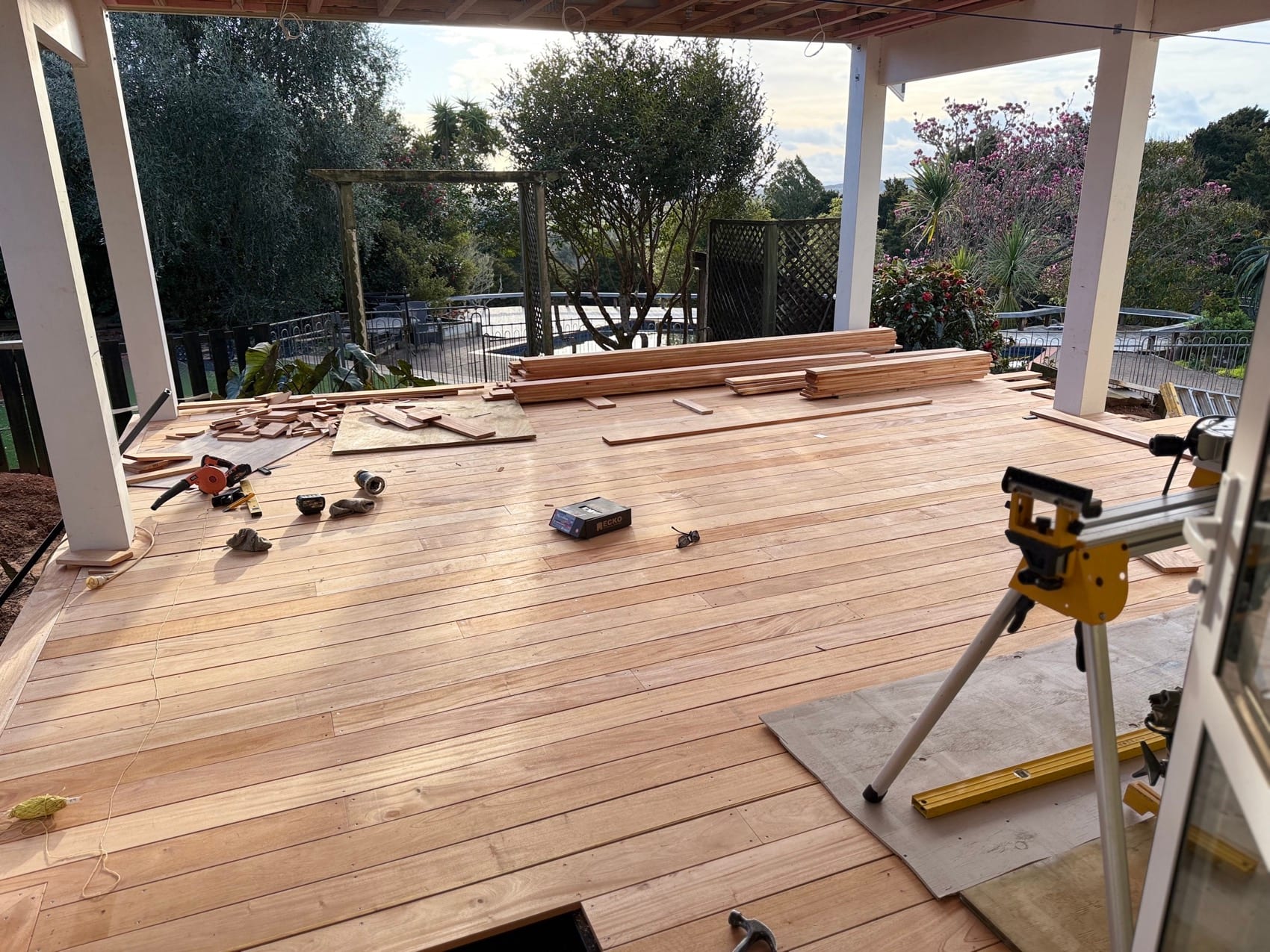 Decking boards being laid over joists, with a drop saw and square set up on the deck.