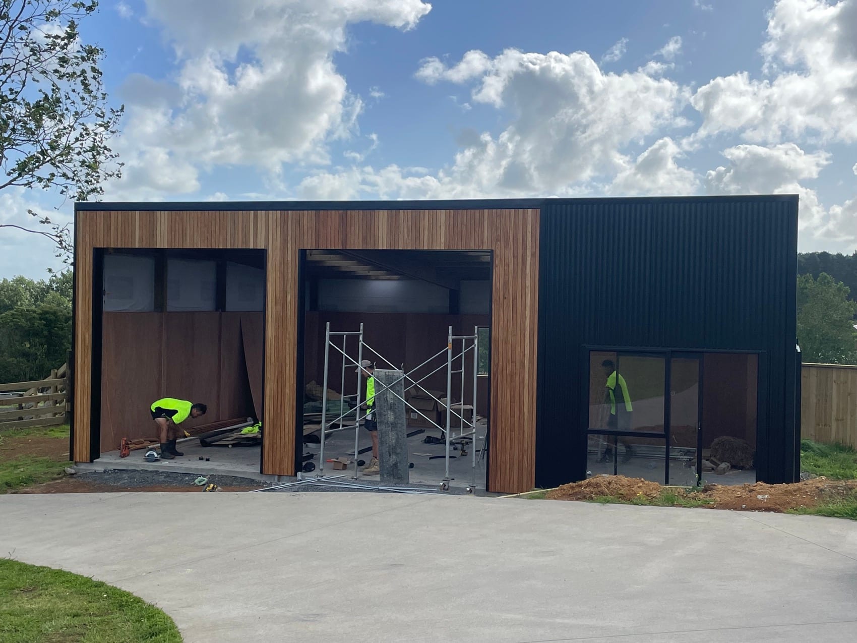 A standalone building by Backline Construction clad in cedar and dark board, with wide openings and a flat roof.
