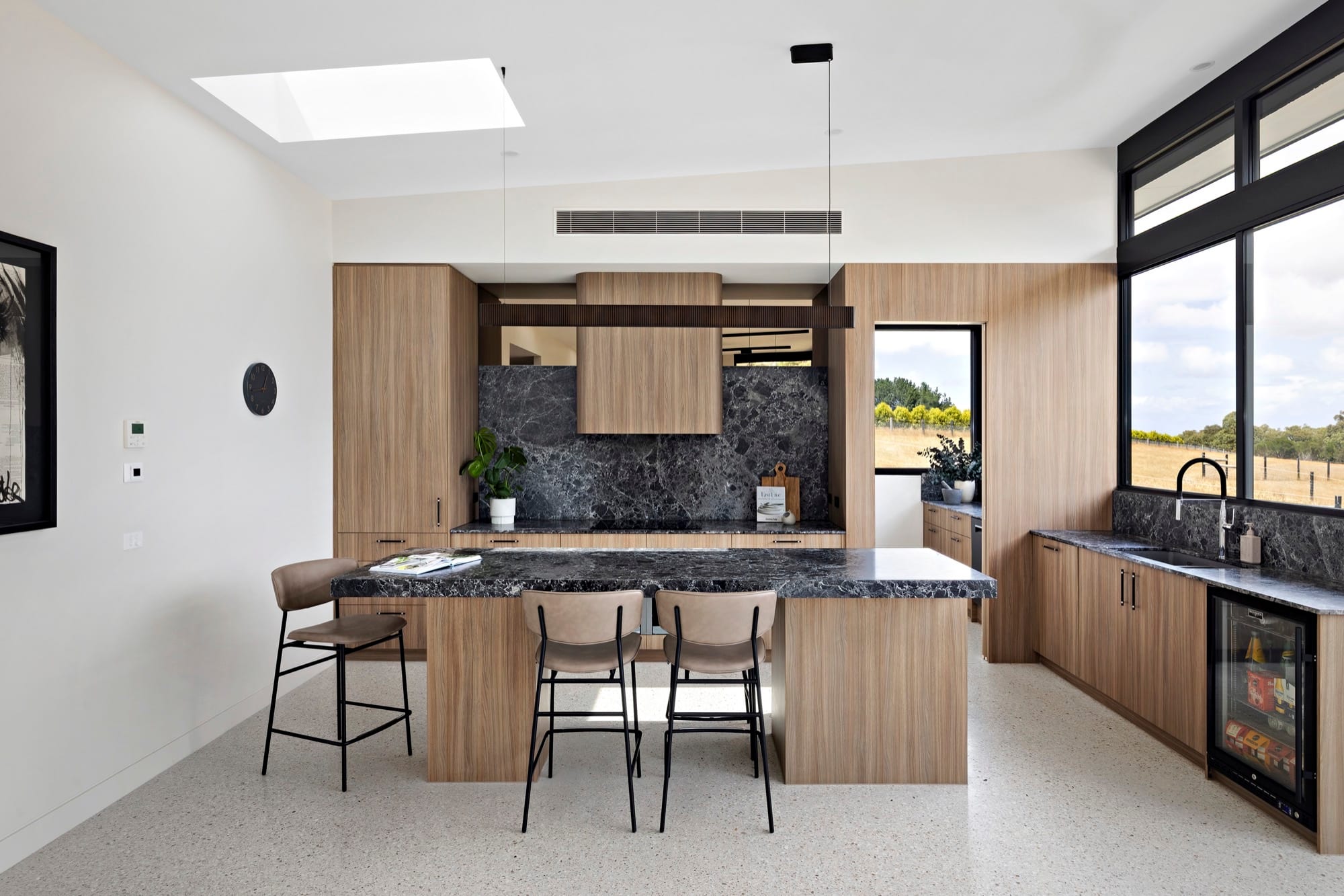 A kitchen with timber cabinetry, a stone benchtop and an integrated sink, lit from a window to one side.