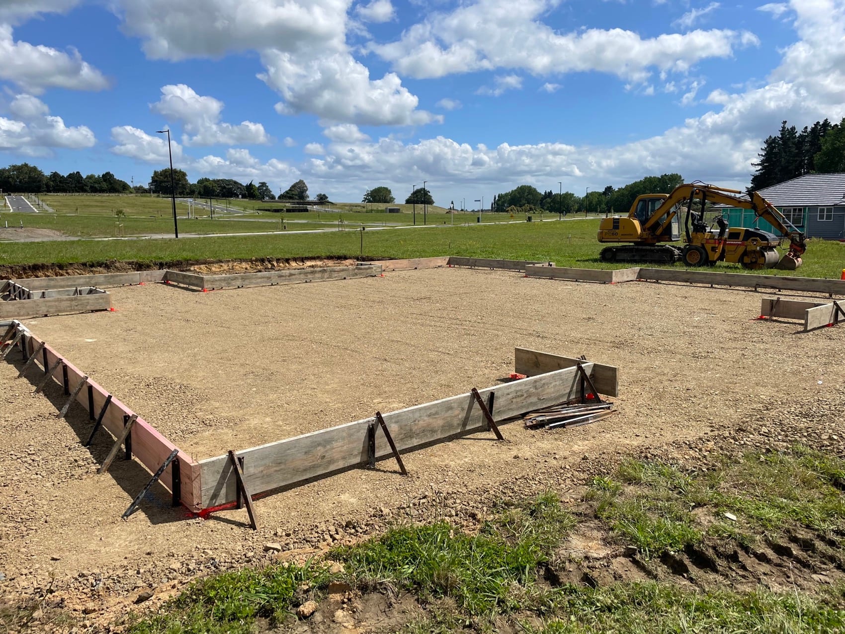 A site prepared and boxed out for foundations with an excavator working at the far end.
