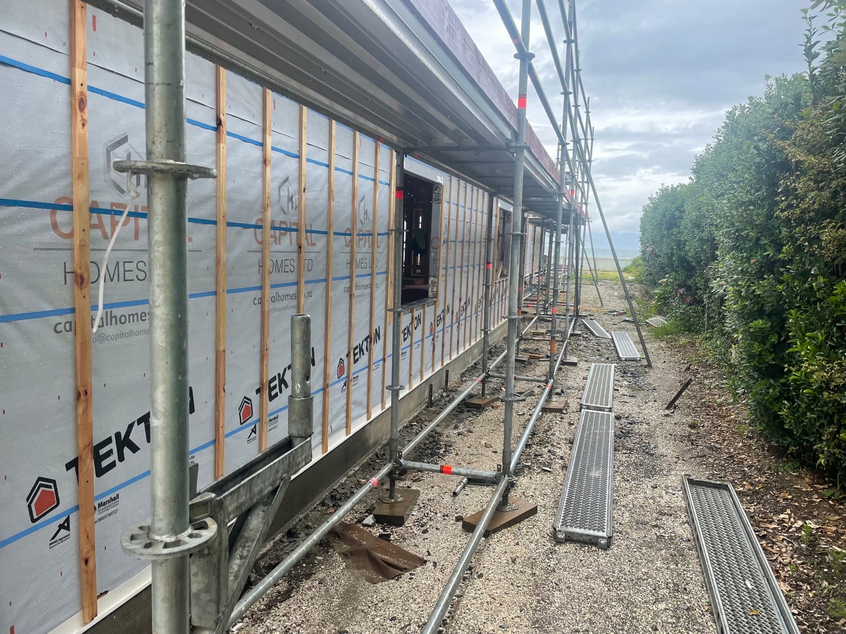 A long elevation at weathertight stage: building wrap taped and sealed, scaffolding up, window openings formed.